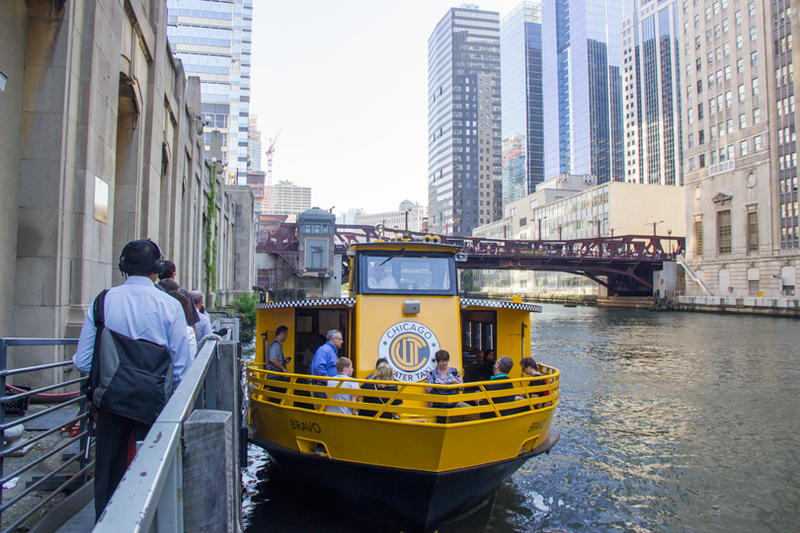 Commuters boarding a yellow Chicago Water Taxi at a downtown river dock
