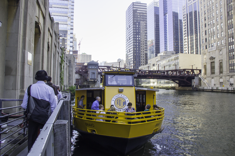 Commuters boarding a yellow Chicago Water Taxi at a downtown river dock